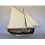 A wooden model of a 19th century fishing boat with three sails and a black painted hull, raised on a