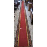 A extremally long machine made red ground wool runner with repeating running border 11.6m long x