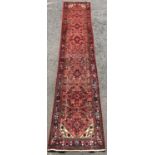 A Malayer Runner with a stylised floral pattern on a pink ground, 400cm x 80cm approx