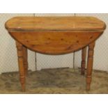A rustic stripped pine oval drop leaf kitchen table with tongue and groove boarded top raised on