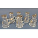 Six miniature glass decanters with silver flip over lids, each with a loose silver whisky label