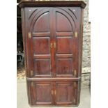 A large Georgian oak floorstanding corner cupboard enclosed by two pairs of fielded panelled doors