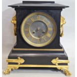 A Victorian black slate and gilded brass overlaid mantle clock with lion mask and ring handles and