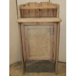 A small rustic stripped pine side cupboard enclosed by a rectangular panelled door beneath a