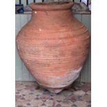 A large antique terracotta olive jar with glazed interior and banded detail, raised on a low iron