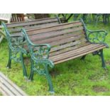 A pair of two seat garden benches with stained wooden lathes raised on decorative pierced green