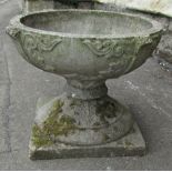 A weathered cast composition stone two sectional garden urn, the squat circular bowl with