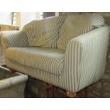 A two seat sofa with shaped outline and repeating green and cream upholstered finish raised on squat