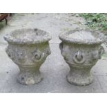 A pair of small weathered cast composition stone garden urns with repeating lions mask and ring