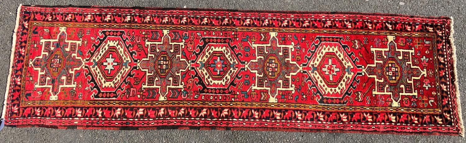 A Heriz runner with a single row interlocking shaped medallions on a predominantly red ground, 275cm