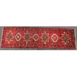 A Heriz runner with a single row interlocking shaped medallions on a predominantly red ground, 275cm