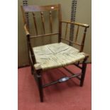 A 19th century beech and ash wood spindle back elbow chair with rush seat on turned supports
