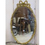 A decorative oval gilt framed mirror with ribboned and repeating floral detail enclosing a