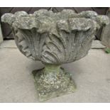 A weathered cast composition stone garden urn with circular acanthus leaf bowl and loose socle