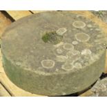 A weathered natural stone millstone with circular central cut out, 56 cm diameter x 15 cm thick
