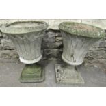 Two similar weathered cast composition stone garden urns of circular tapered form with flared