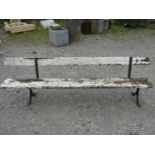 An old platform bench with painted and weathered wooden plank seat and back rail, raised on cast