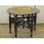 An Eastern embossed Benares type circular tray top occasional table raised on a chip carved ebonised