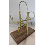 A vintage mechanical brass wine cradle, raised on a wooden base.