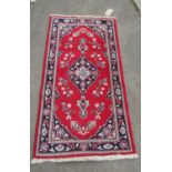 A small Tabriz mat with a central medallion and floral decorations on red ground, 130cm x 70cm
