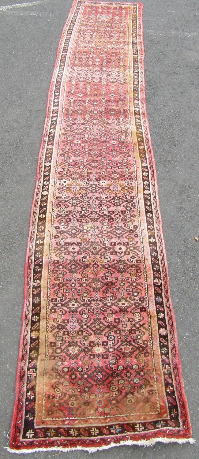 A Hamadan runner with a repeating geometric pattern on a predominantly pink ground, 500cm x 88cm.