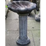 A weathered cast composition stone bird bath, the scallop shell shaped bowl raised on a fluted