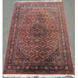 A Persian design carpet with a central medallion and all over floral pattern on a rusty red ground
