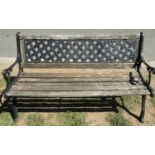 A garden bench with weathered timber slatted seat beneath a decorative cast iron lattice pattern