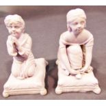 A pair of Minton figures of crouching and praying children seated upon cushions, in a lilac