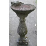 A weathered cast composition stone bird bath with baluster shaped pedestals supporting a shell