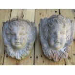 A pair of weathered cast composition stone garden wall pockets with cherub mask detail, 24 cm high x