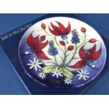 A Moorcroft Pottery year plate decorated with red lilies, cosmos and bluebells and date 2001,