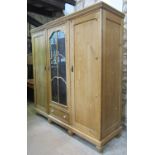 A continental stripped pine wardrobe enclosed by three panelled doors, the central glazed with