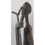 African bronze sculpture of an elongated figure of a man holding a walking stick raised on a stepped