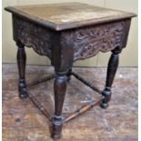 An Old English oak stool with repeating carved foliated detail, raised on turned supports and rails,