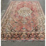 A Persian Kashan carpet with with a central medallion with an all over floral pattern on a faded red