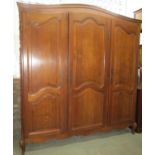 An oak armoire enclosed by three fielded panelled doors flanked by panelled sides beneath a domed