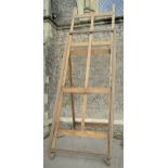 An outsized oak picture easel with hinged framework, 3.8m tall x 1.2m wide