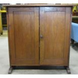 An oak Arts & Crafts style side cupboard, freestanding and enclosed by a pair of rectangular