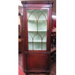 A Georgian mahogany free standing corner cupboard, the lower section enclosed by a panelled door,
