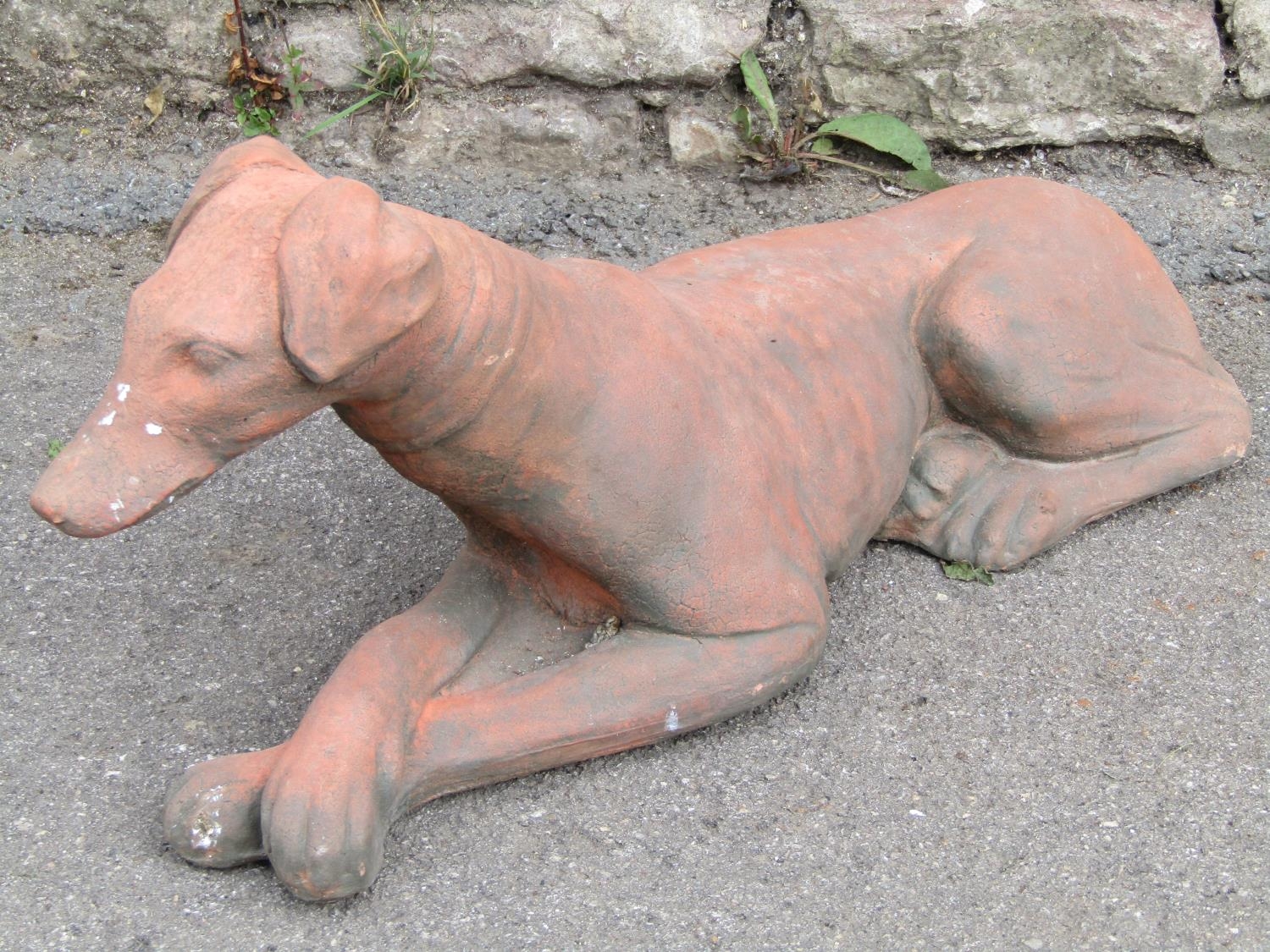 A cast composition stone garden ornament in the form of a recumbent greyhound/whippet with