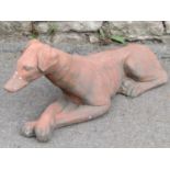 A cast composition stone garden ornament in the form of a recumbent greyhound/whippet with