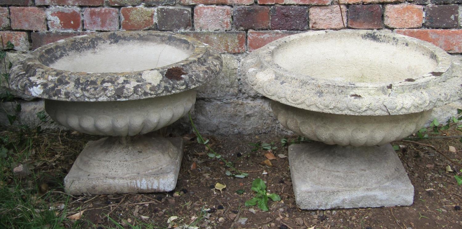 A pair of weathered cast composition stone garden urns, squat circular bowls with flared egg and