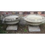 A pair of weathered cast composition stone garden urns, squat circular bowls with flared egg and