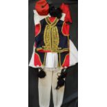 Greek traditional man's costume comprising braided waistcoat, white legwear, red sash, tasselled hat