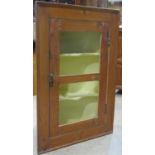 A stripped pine hanging corner cabinet enclosed by a rectangular segmented panelled door revealing