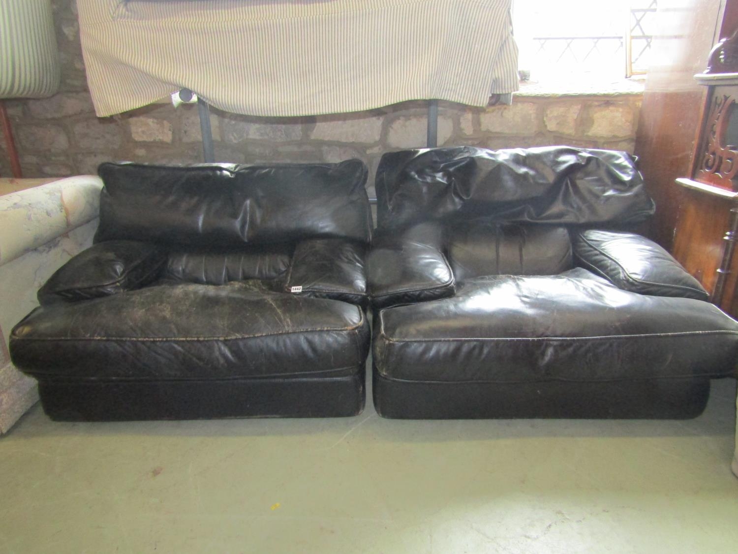 A pair of low substantial easy chairs with soft black leather upholstered finish and loose shaped