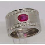 18ct white gold band ring set with an oval ruby and two rows of diamonds, size K/L, 8.9g