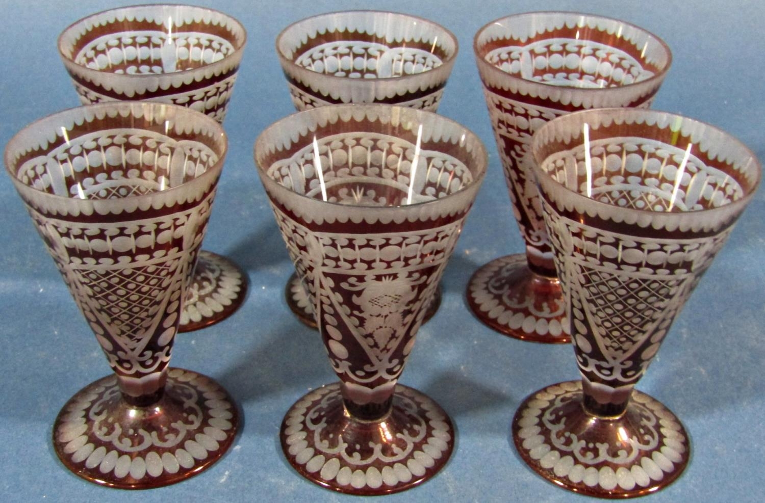 Six red engraved conical shaped liqueur glasses.