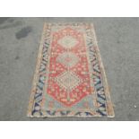 An old Middle Eastern rug with three interlocking medallions on a red ground, 170cm x 90cm